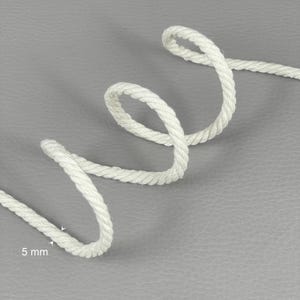 Op de afbeelding: Close-up van een wit, gedraaid touw met een diameter van 5 mm. Het touw is in een luspatroon gerangschikt tegen een grijze achtergrond. De textuur van het touw is zichtbaar, wat de constructie benadrukt. Geschikt voor knutselwerk en nautische projecten.