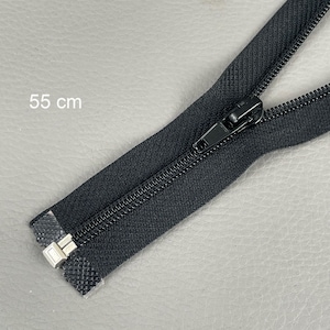 Puede incluir: Cremallera negra de 55 cm de largo, con tirador negro y extremo metálico plateado. La cremallera se muestra sobre una superficie gris claro. El texto "55 cm" es visible.