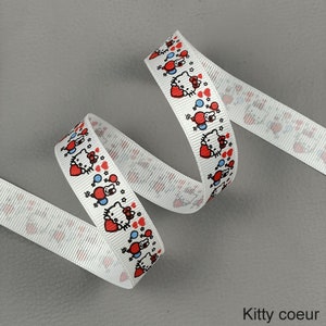 Pode incluir: Fita branca com um padrão repetido de um gato de desenho animado com um coração vermelho, balões azuis e estrelas. A fita é enrolada e tem o texto "Kitty coeur" na parte inferior.