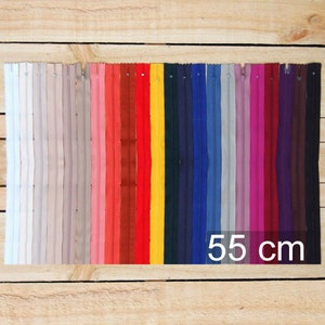 May include: A collection of colorful 55 cm zippers arranged in a row. The zippers span a wide spectrum of colors, including white, gray, pink, red, yellow, blue, and purple. The zippers are displayed on a wooden surface.