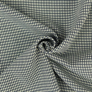 Pode incluir: Close-up de um tecido vichy azul marinho e branco. O tecido tem um padrão xadrez clássico. O material é drapeado e dobrado, criando textura. Ideal para projetos de costura.