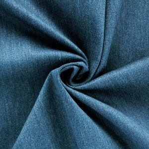 Może przedstawiać: Zbliżenie na próbkę tkaniny dżinsowej w głębokim niebieskim odcieniu. Tkanina jest gęsto tkana, z lekko teksturowaną powierzchnią. Materiał jest złożony i udrapowany, tworząc miękkie cienie i podkreślając fakturę i kolor tkaniny.