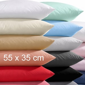 Könnte beinhalten: Ein Stapel rechteckiger Kissen in verschiedenen Unifarben wie Weiß, Mintgrün, Hellblau, Beige, Pfirsich, Rot, Schwarz und Rosa. Der Text 55 x 35 cm ist auf das pfirsichfarbene Kissen gedruckt. Die Kissen haben eine glatte, einfarbige Stoffoberfläche.
