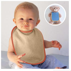 Pode incluir: Um babete bege com acabamento laranja é usado por um bebé. O babete é feito de um material macio e absorvente. Um pequeno ursinho de peluche com um babete azul está no fundo.