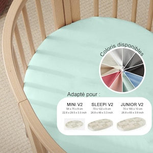 Peut inclure: Un drap-housse vert clair pour lit bébé, présenté sur un cadre de lit en bois. L'image comprend une palette de couleurs et des informations de taille pour MINI V2 (58 x 75 x 9 cm), SLEEPI V2 (70 x 122 x 9 cm) et JUNIOR V2 (70 x 165 x 10 cm).