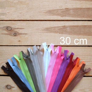Puede incluir: Una colección de cremalleras de 30 cm en varios colores, dispuestas en forma de abanico. Los colores incluyen negro, azul, verde, gris, blanco, rosa, morado, rojo y naranja. El texto "30 cm" está en blanco.