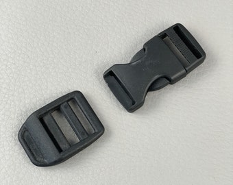 May include: Two black plastic side-release buckles. One buckle is open, showing the male and female parts separated. The other buckle is closed, showing the two parts connected. The buckles are on a light grey surface.