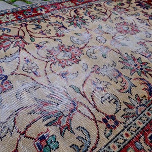 May include: A vintage rug with a cream background and intricate floral patterns in shades of red, blue, and green. The rug has a worn and faded appearance, adding to its vintage charm.