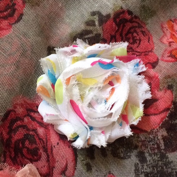 Broche fleur multicolore sur fond blanc, à pois en tissu de mousseline effiloché, shabby trashy, gaieté d'été.