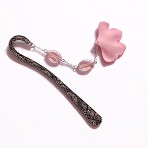Peut inclure: Un marque-page argenté avec un motif floral et un charme de fleur rose. Le marque-page a deux perles de verre roses sur une chaîne argentée.
