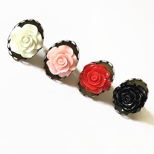 Può includere: Quattro anelli con rose di diversi colori. Gli anelli sono in metallo con un bordo decorativo e presentano una rosa bianca, rosa, rossa e nera.