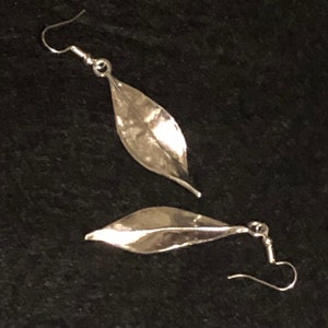 Può includere: Un paio di orecchini a forma di foglia d'argento con una texture martellata. Gli orecchini sono di stile pendente con chiusura a gancio.