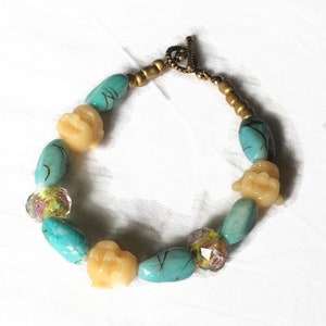 Bracelet fantaisiste à têtes de Bouddha hilares dans un jardin rose, jaune, vert, transparent sous un ciel turquoise, apprêts vieil or image 1