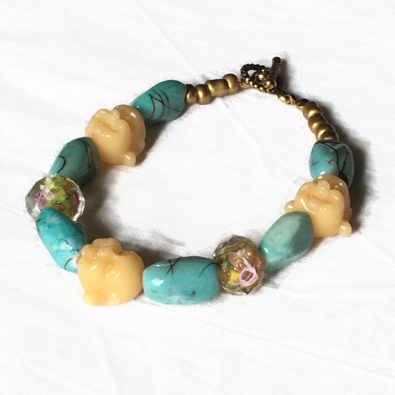 Bracelet fantaisiste à têtes de Bouddha hilares dans un jardin rose, jaune, vert, transparent sous un ciel turquoise, apprêts vieil or image 2