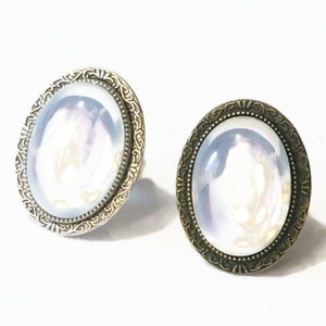 Peut inclure: Deux bagues ovales avec des pierres en verre irisées serties dans des montures ornées d'argent et de bronze.