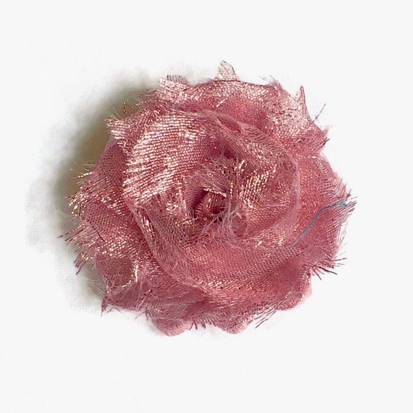 Viejo broche de flores rosa metálico brillante en tela de muselina deshilachada en forma de remolino, basura en mal estado, rosa salvaje.