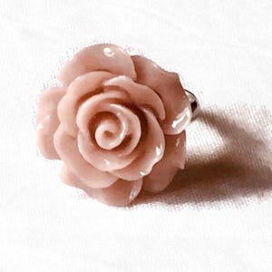 Könnte beinhalten: Ein Ring mit einer rosafarbenen Rose und einem silbernen Band. Die Rose ist aus einem glatten, glänzenden Material gefertigt und wirkt realistisch.