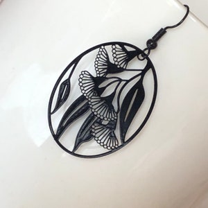 Peut inclure: Boucles d'oreilles pendantes noires avec un motif découpé de feuilles et de fleurs d'eucalyptus.