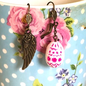 Asymmetrical sleeper earrings with white egg, fuchsia 3D patterns in Bohemian glass and two-sided bronze angel wing decorated with a rose