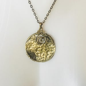Peut inclure: Collier pendentif de couleur bronze avec un pendentif circulaire texturé. Le pendentif présente un motif en spirale au centre et des accents de fil enroulé. La chaîne est de couleur bronze assortie, créant un accessoire d'inspiration vintage.