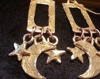 May include: Gold tone earrings with a crescent moon and star charm hanging from a rectangular pendant.