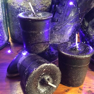 May include: Three black pillar candles with white wicks, sitting on a wooden surface with a string of purple fairy lights.