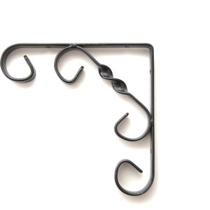 May include: Black metal corner shelf bracket with decorative scrollwork. The bracket has three hooks for hanging items.