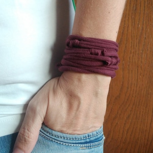 Könnte beinhalten: Nahaufnahme eines Handgelenks, das ein burgunderfarbenes Stoffarmband trägt. Das Armband besteht aus mehreren Stofflagen, die einen dicken und strukturierten Look erzeugen.