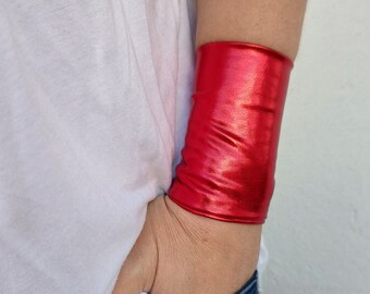 Puede incluir: Un brazalete de muñeca rojo metálico. El brazalete está hecho de un material brillante y flexible.