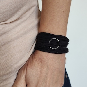 May include: Black fabric bracelet with a large silver circle accent.  "Black - Big Circle" is written below the bracelet.