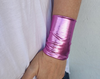 Op de afbeelding: Een roze metalen polsband. De polsband is gemaakt van een glanzend, reflecterend materiaal.