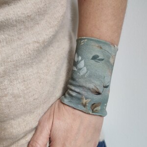 Op de afbeelding: Een groene polsband met een bloemenpatroon. Het patroon heeft witte en bruine bladeren en bloemen. De tekst "Early Spring" is zichtbaar onderaan de afbeelding.