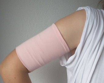 Op de afbeelding: Een roze stoffen armbeschermer gedragen op de bovenarm van een persoon.