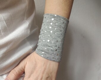 Può includere: Bracciale da polso grigio con punti argentati. Il bracciale è realizzato in tessuto morbido ed elastico, perfetto per aggiungere un tocco di brillantezza a qualsiasi outfit.