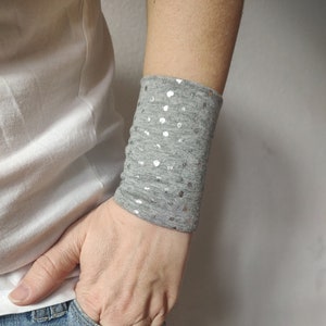 Può includere: Bracciale da polso grigio con punti argentati. Il bracciale è realizzato in tessuto morbido ed elastico, perfetto per aggiungere un tocco di brillantezza a qualsiasi outfit.