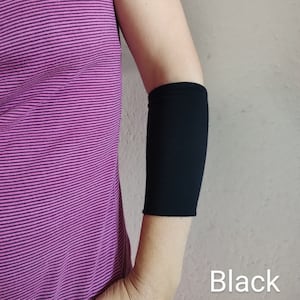 Peut inclure: Manche de coude noire en tissu extensible. La manche est portée sur le bras gauche. Noir.