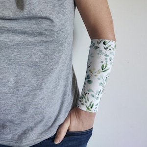 May include: A white arm sleeve with a green floral pattern. The sleeve is made of a soft, stretchy fabric and is ideal for protecting your skin from the sun.
