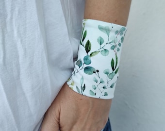 Può includere: Un braccialetto bianco per il polso con un motivo a foglie di eucalipto verdi. Il braccialetto è realizzato in tessuto e ha un design semplice.