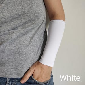 May include: A white arm sleeve is displayed on an arm. The sleeve is made of a smooth, opaque fabric. The word "White" is written in the bottom right corner of the image. The person is wearing a grey t-shirt and blue jeans.