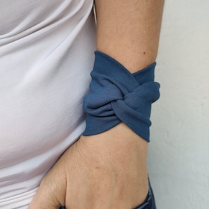 May include: A blue fabric wrist cuff with a knotted design. The cuff is made of a soft, stretchy material and is comfortable to wear. Indigo.