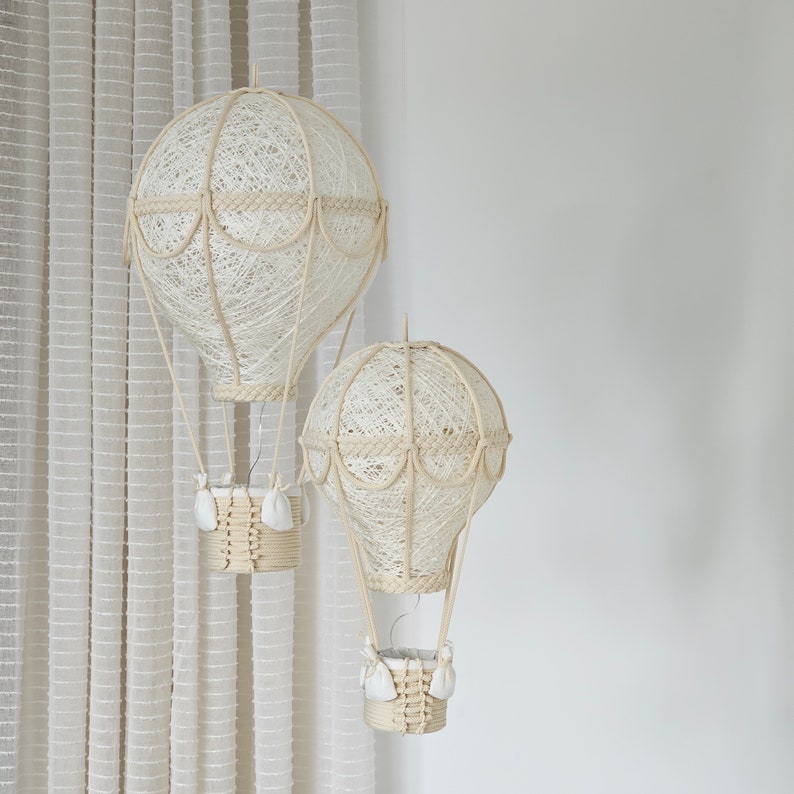 May include: Two white, string-wrapped hot air balloons with wicker baskets hanging from them. The larger balloon is on the left and the smaller balloon is on the right.