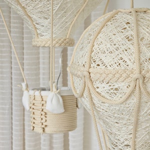 May include: Two white string hot air balloons with a basket made of woven rope. The balloons are hanging from the ceiling.