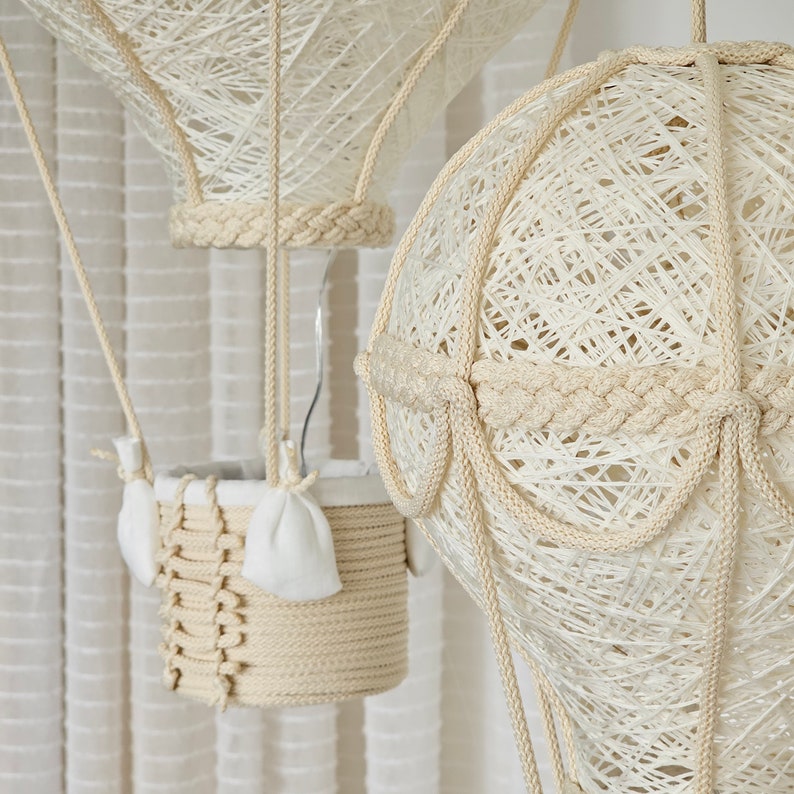 May include: Two white string hot air balloons with a basket made of woven rope. The balloons are hanging from the ceiling.