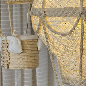 May include: Three white string hot air balloons with lights inside. The balloons are hanging from the ceiling and have a woven rope design.