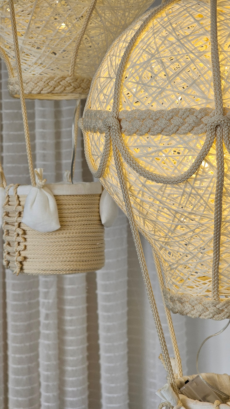 May include: Three white string hot air balloons with lights inside. The balloons are hanging from the ceiling and have a woven rope design.