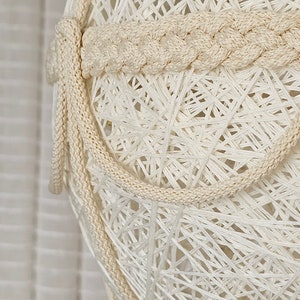 May include: A white string light with a braided rope detail. The light is made of a delicate, woven material and has a natural, rustic look.