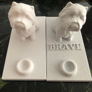Pode incluir: Dois suportes de livros brancos em forma de cão. Um tem uma pequena reentrância redonda, e o outro a palavra "BRAVE" em maiúsculas. Ambos têm uma pequena reentrância redonda.