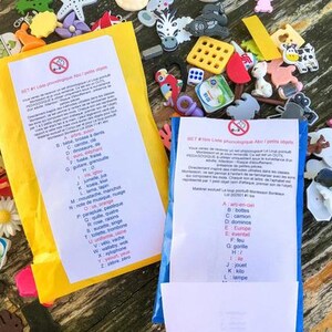 Könnte beinhalten: Zwei gelbe und blaue Umschläge mit pädagogischen phonologischen Listen und kleinen Kunststofffiguren. Die Listen enthalten französischen Text, der nach Buchstaben geordnet ist, begleitet von einer Vielzahl bunter Miniaturobjekte wie Tiere, Lebensmittel und Formen, die um die Umschläge herum verstreut sind.