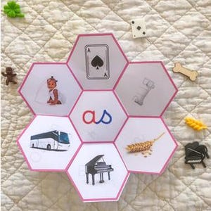 Peut inclure: Une carte d'apprentissage hexagonale présentant les lettres 'as' au centre, entourées de six petits hexagones illustrant une carte as, un lit, un épi de blé, un piano à queue, un bus et un enfant.