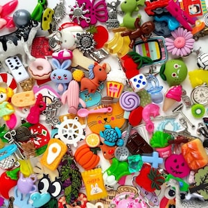 May include: A vibrant collection of small decorative charms and embellishments. The assortment features diverse shapes and themes, including animals, food items, and geometric designs. The charms are made from various materials and in a spectrum of colours.